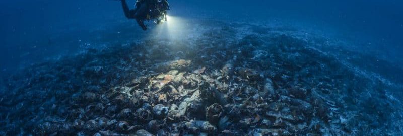 Diver evaluates the remains of the ship covered with hundreds of amphorae